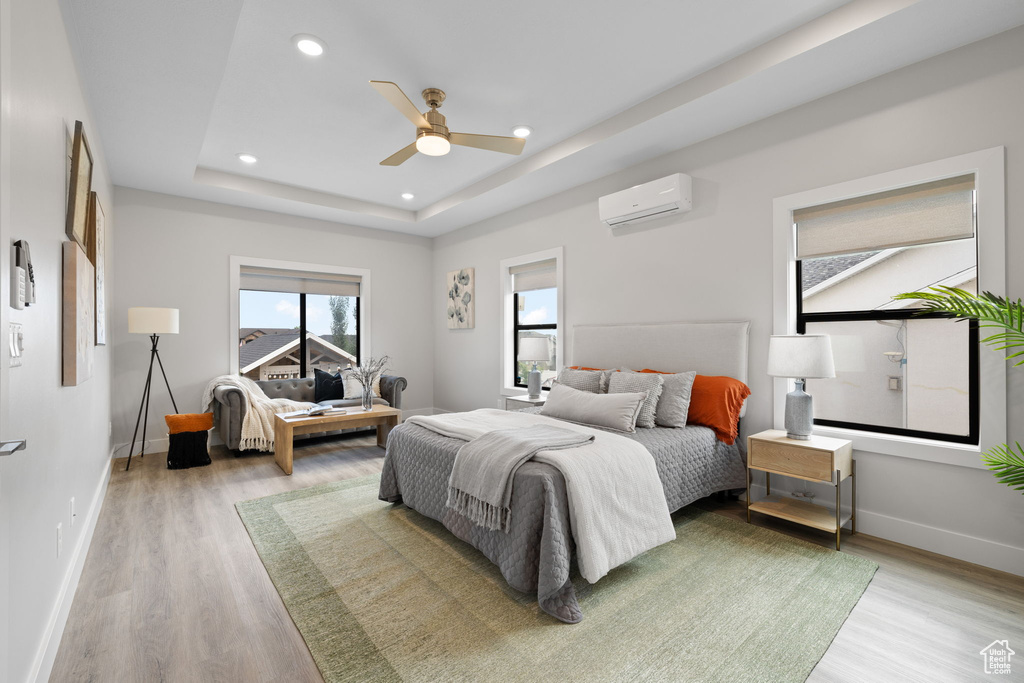 Bedroom featuring light wood-type flooring, recessed lighting, baseboards, a wall unit AC, and a tray ceiling