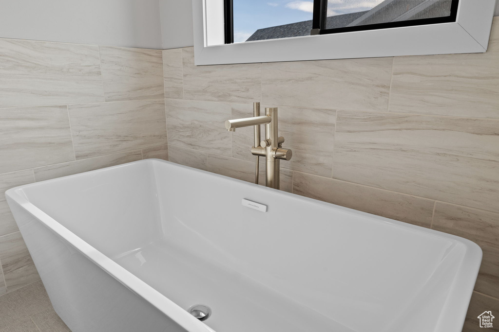 Bathroom featuring tile walls, a soaking tub, and a sink