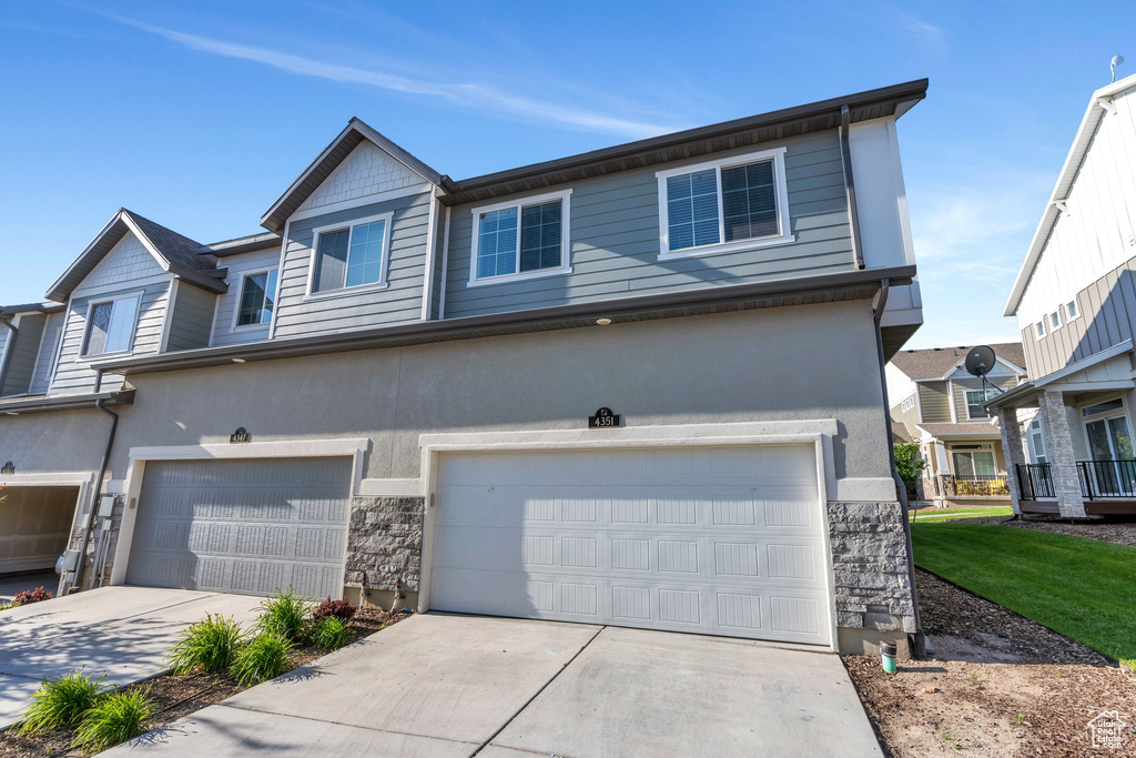 Multi unit property with an attached garage, driveway, stone siding, and stucco siding