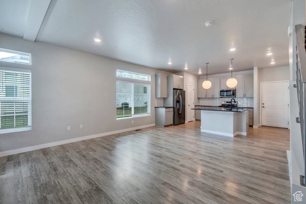 Kitchen with stainless steel appliances, dark countertops, open floor plan, backsplash, and a center island with sink
