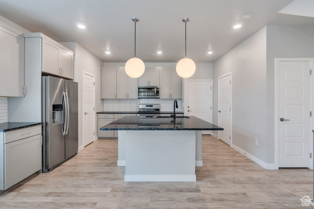 Kitchen with appliances with stainless steel finishes, dark stone countertops, backsplash, light wood finished floors, and recessed lighting