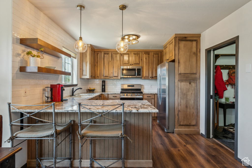 Kitchen with appliances with stainless steel finishes, dark wood finished floors, a sink, a peninsula, and light stone countertops