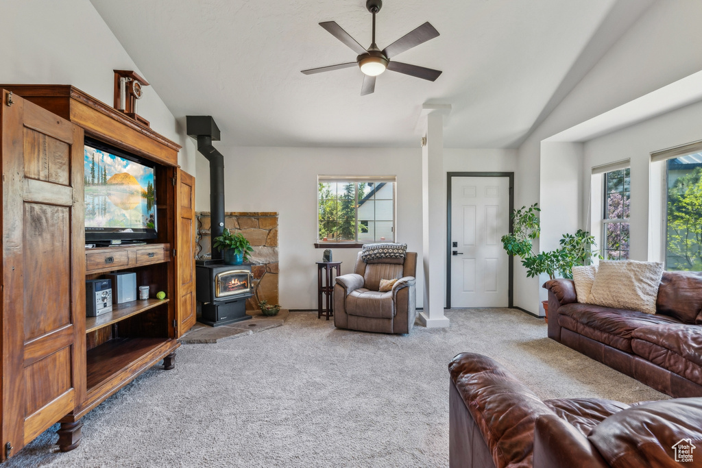 Carpeted living area featuring a wood stove, lofted ceiling, plenty of natural light, and a ceiling fan