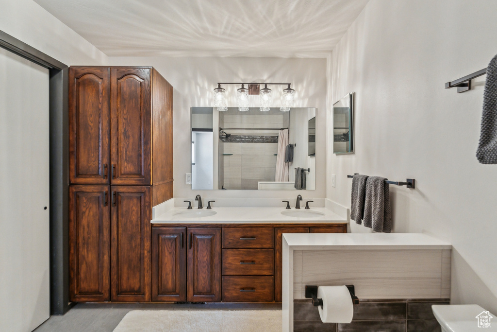 Bathroom with double vanity, tiled shower, and toilet