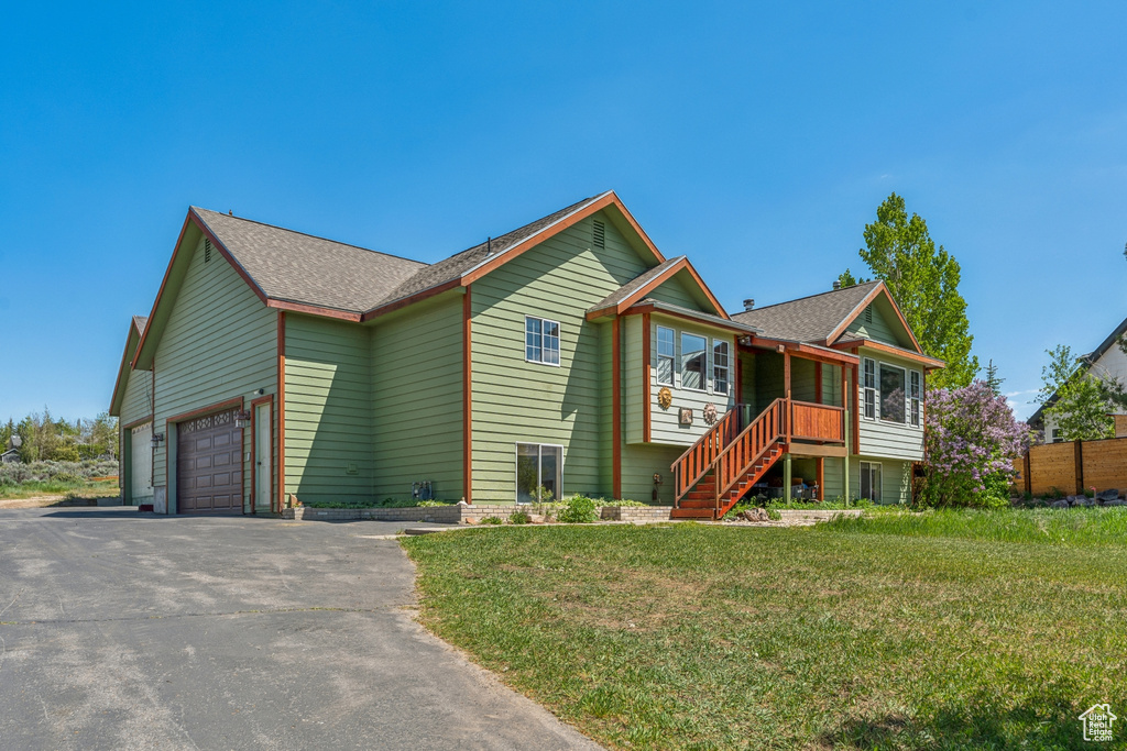 View of front of house with driveway, an attached garage, a front yard, roof with shingles, and stairway