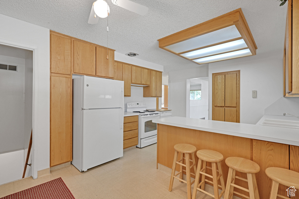 Kitchen with white appliances, a peninsula, ceiling fan, light countertops, and a sink