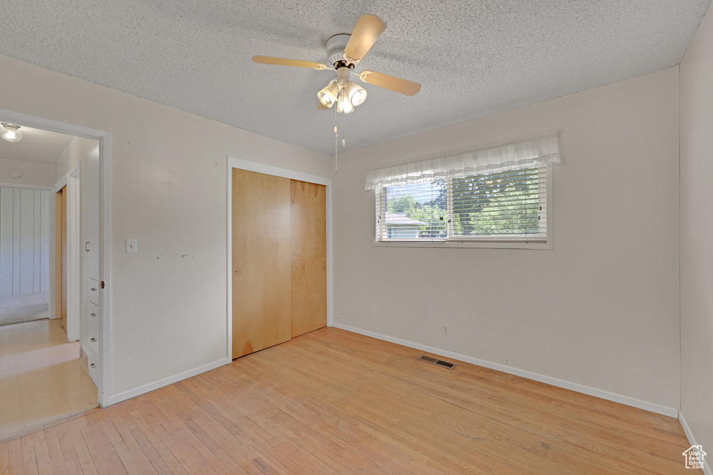 Unfurnished bedroom with baseboards, light wood-type flooring, a closet, a textured ceiling, and ceiling fan