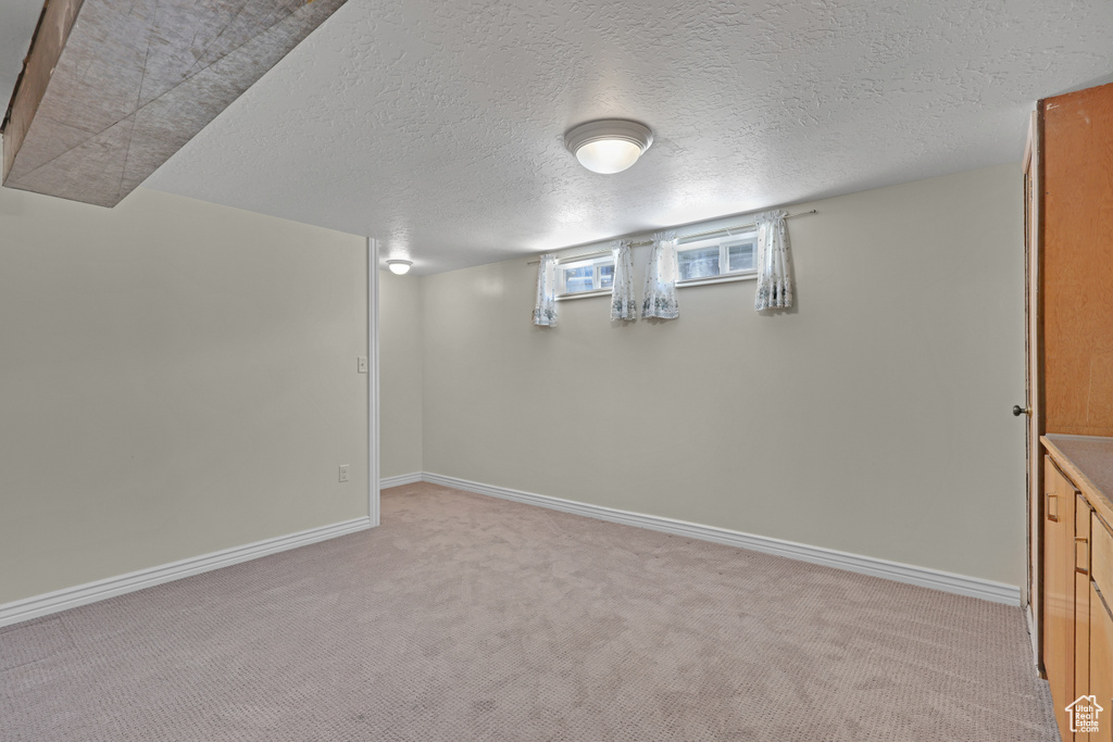 Basement with light colored carpet, baseboards, and a textured ceiling