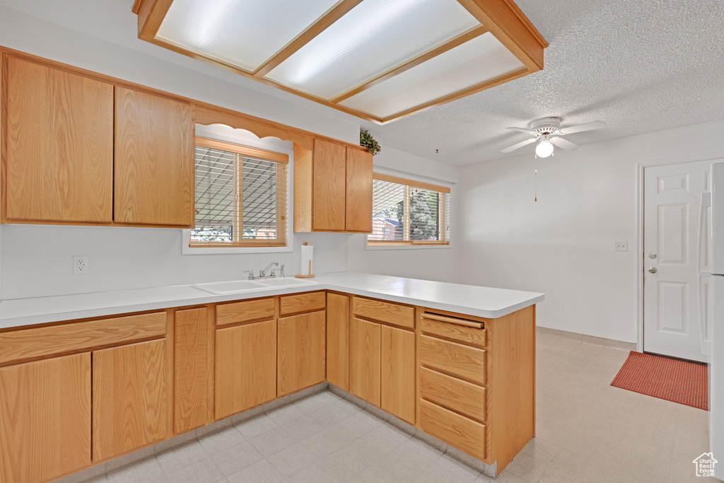 Kitchen with a peninsula, a sink, light floors, light countertops, and a textured ceiling