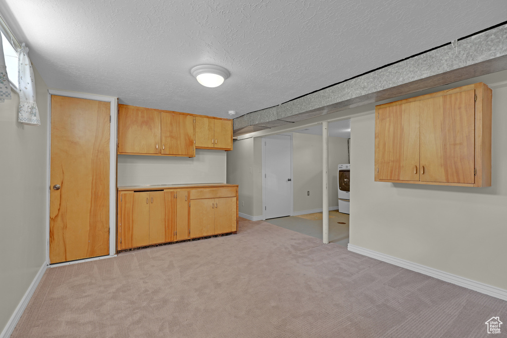 Kitchen featuring a textured ceiling, light colored carpet, baseboards, light countertops, and light brown cabinetry
