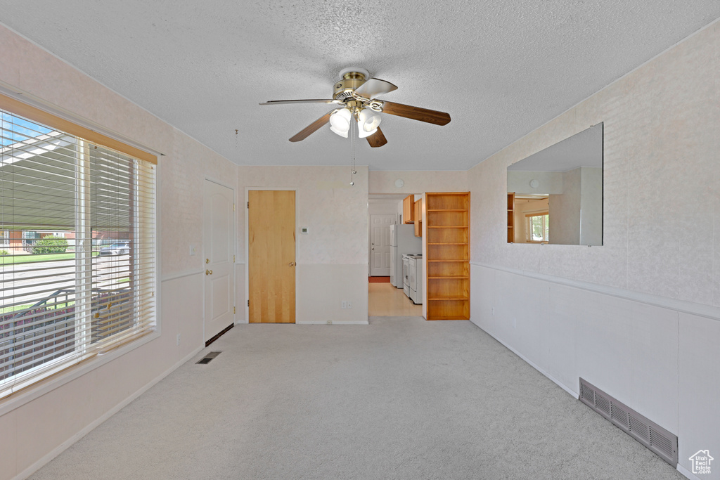 Spare room featuring a ceiling fan, a textured ceiling, healthy amount of natural light, and light colored carpet