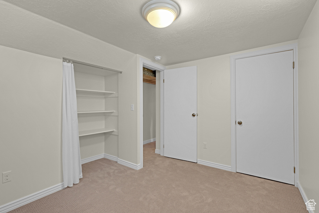 Unfurnished bedroom with light colored carpet, a textured ceiling, baseboards, and a closet