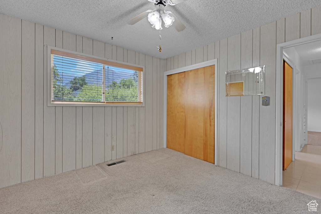 Unfurnished bedroom with a textured ceiling, carpet, wood walls, and ceiling fan