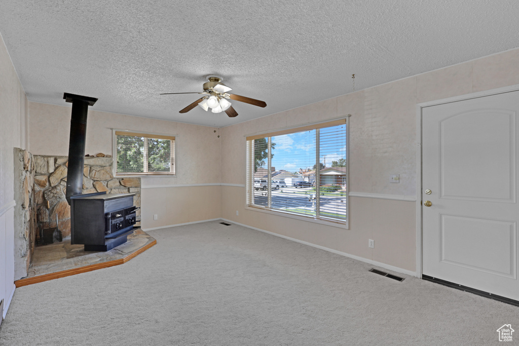 Unfurnished living room featuring a textured ceiling, a ceiling fan, carpet flooring, a wood stove, and baseboards