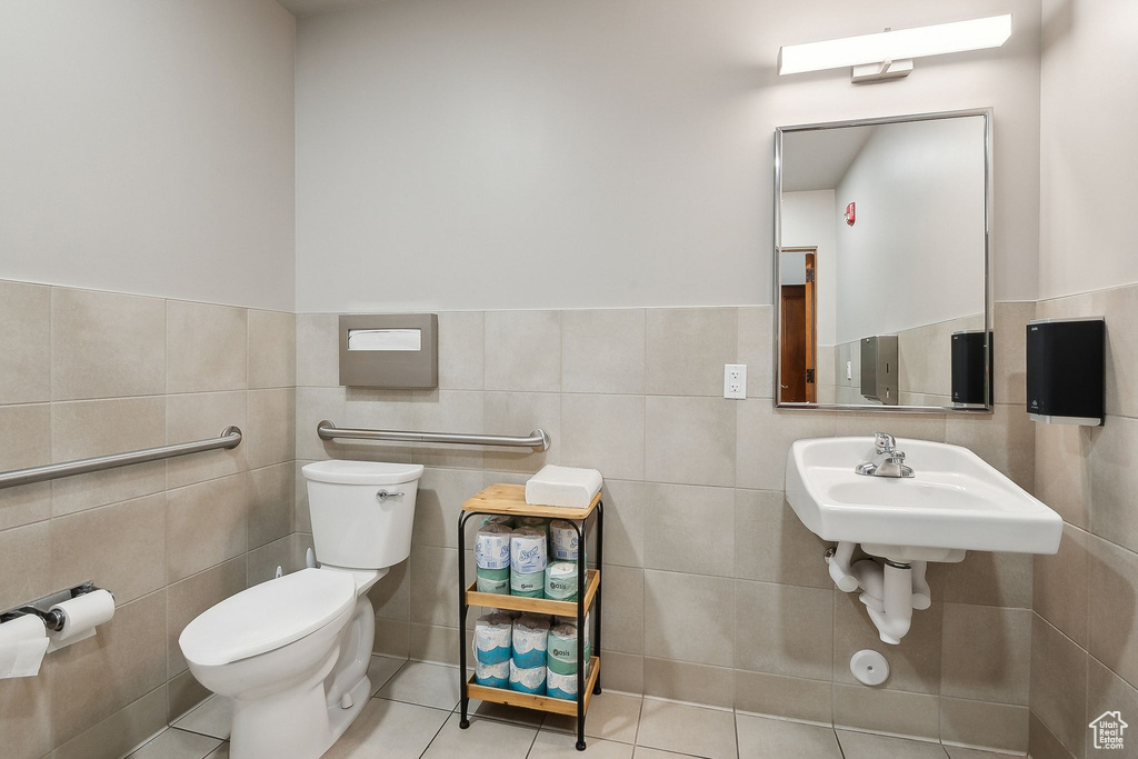 Half bath with toilet, tile patterned flooring, tile walls, wainscoting, and a sink