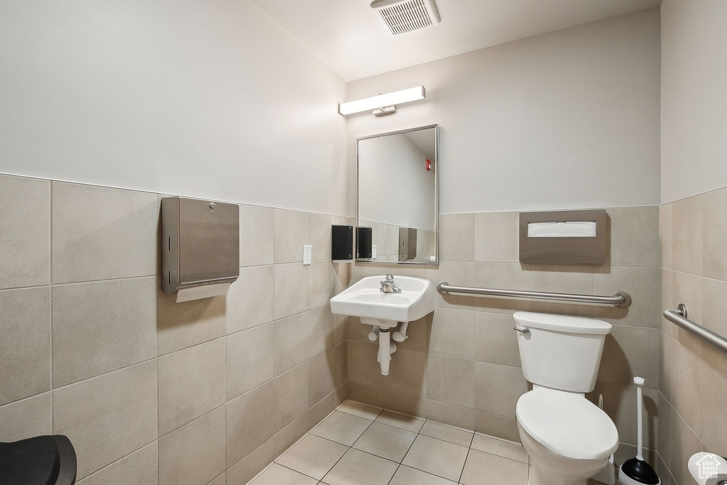 Bathroom featuring toilet, tile patterned floors, tile walls, and a wainscoted wall