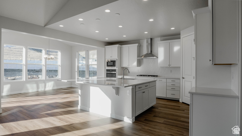 Kitchen with wall chimney exhaust hood, stainless steel appliances, recessed lighting, backsplash, and dark wood-style floors