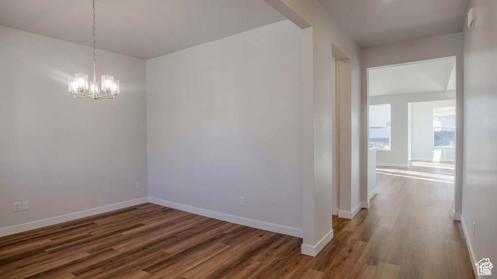 Empty room featuring wood finished floors, a chandelier, and baseboards