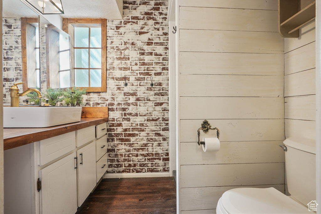 Half bath with wood finished floors, toilet, vanity, baseboards, and brick wall