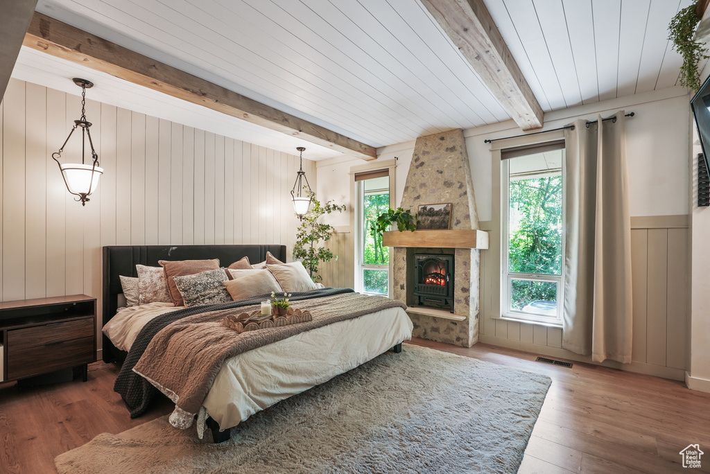 Bedroom featuring beam ceiling, wood finished floors, a stone fireplace, and wood walls