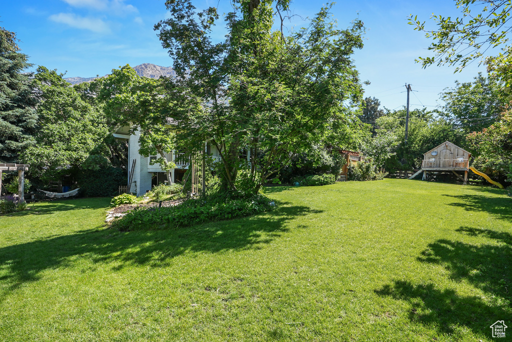 View of grassy yard with a playground and a mountain view