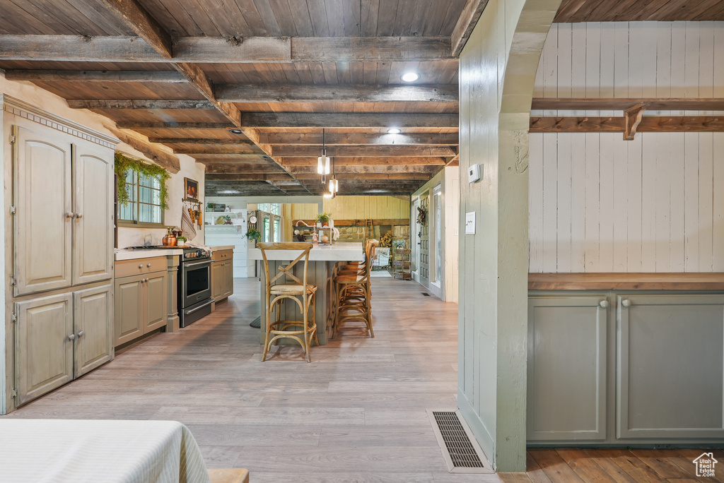 Kitchen with stainless steel stove, wood ceiling with exposed beams, light wood finished floors, wooden walls, and a breakfast bar area