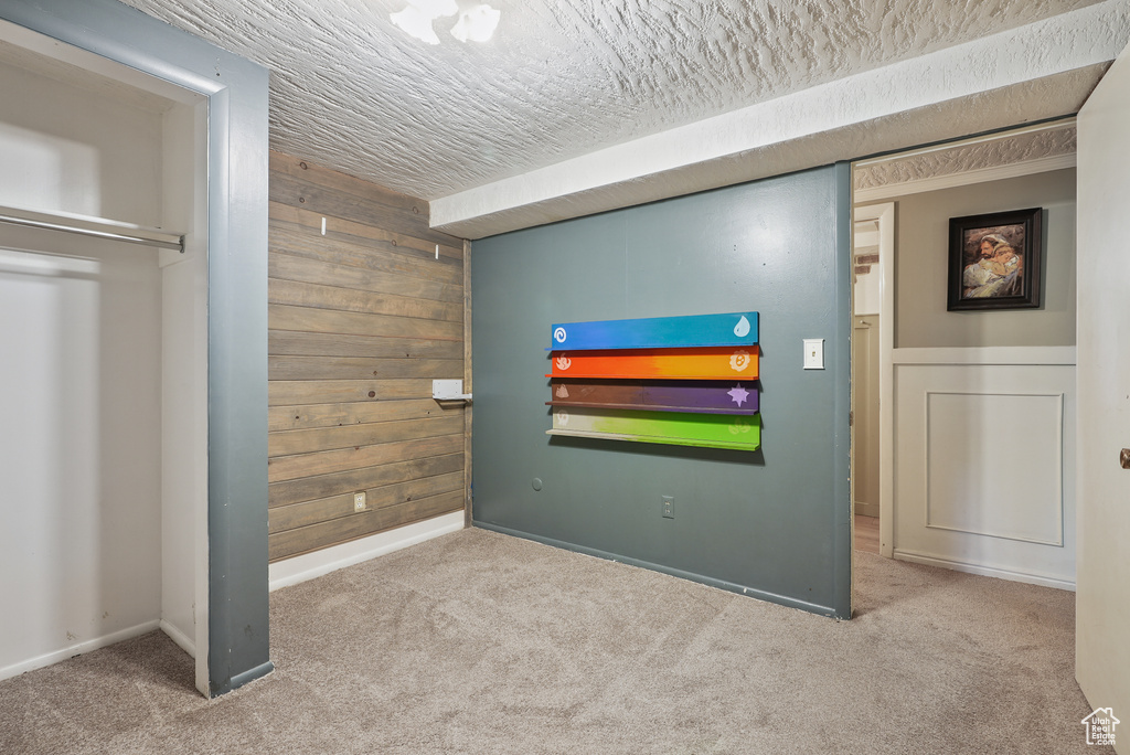Unfurnished bedroom with carpet floors, wooden walls, a textured ceiling, and baseboards