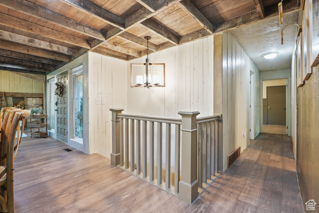 Hall featuring wood finished floors, wood ceiling with exposed beams, an upstairs landing, wood walls, and a chandelier