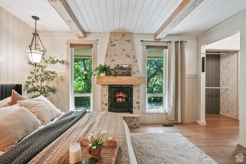 Living room featuring plenty of natural light, wood finished floors, a large fireplace, a wainscoted wall, and wooden ceiling with exposed beams