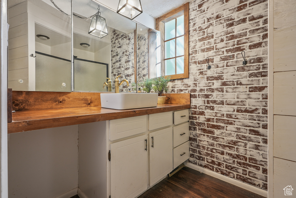 Bathroom with wood finished floors, vanity, baseboards, a stall shower, and brick wall