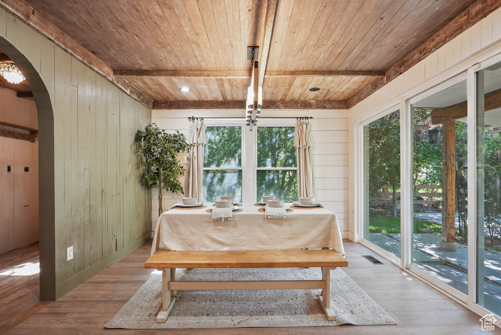 Dining room featuring wooden ceiling with exposed beams, arched walkways, wood walls, and wood finished floors