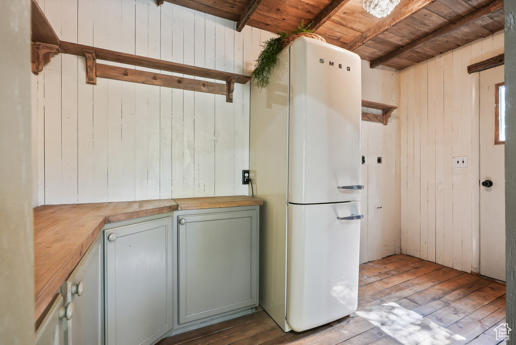 Kitchen with freestanding refrigerator, wood counters, wood ceiling with exposed beams, hardwood / wood-style flooring, and wood walls
