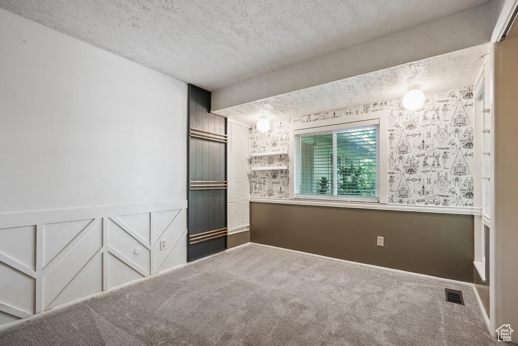 Carpeted spare room featuring a textured ceiling and wainscoting