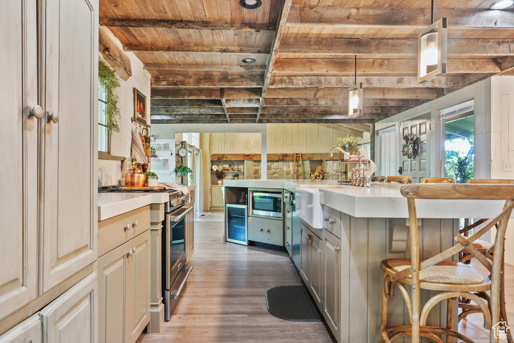Kitchen with wooden ceiling with exposed beams, stainless steel appliances, a sink, wood finished floors, and light countertops