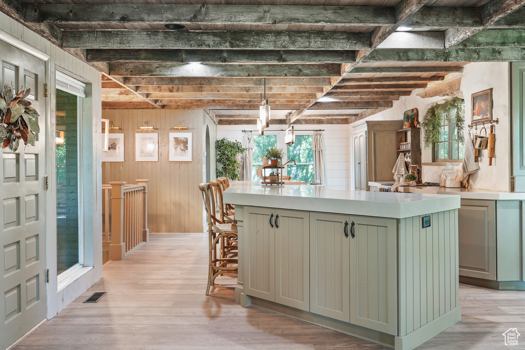 Kitchen with green cabinetry, a center island, light wood finished floors, light countertops, and beamed ceiling
