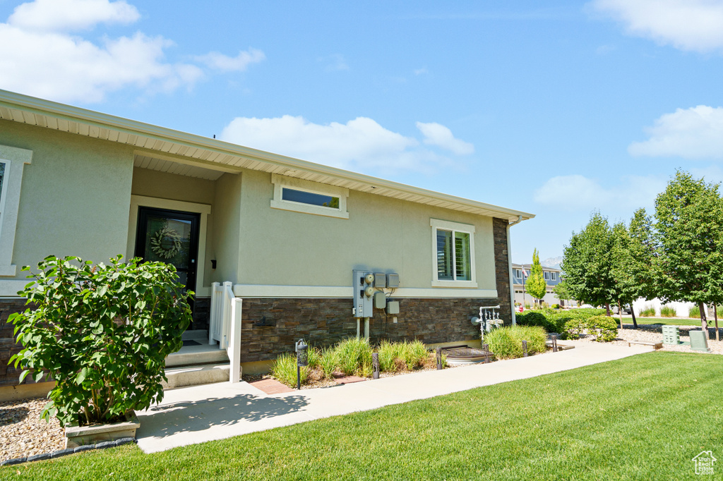 View of property exterior with stucco siding, stone siding, and a yard