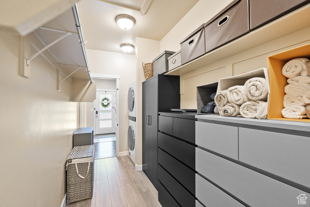 Walk in closet with stacked washer and clothes dryer and light wood-type flooring