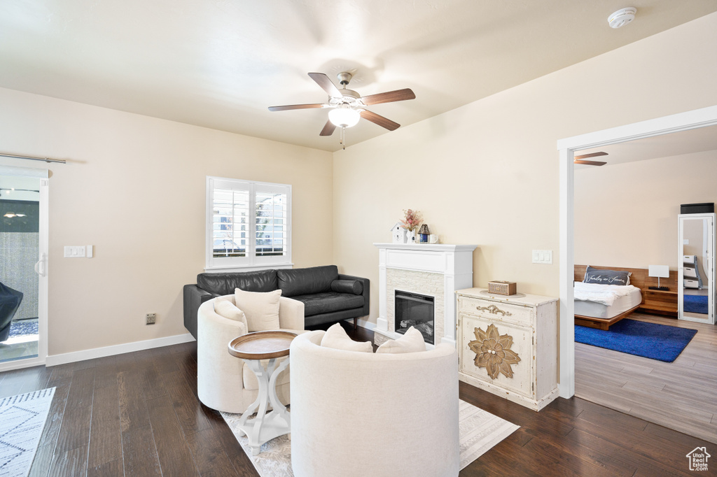 Living area featuring ceiling fan, dark wood finished floors, a glass covered fireplace, and baseboards