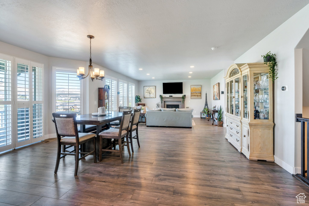 Dining room featuring dark wood-style floors, recessed lighting, a chandelier, a fireplace, and baseboards