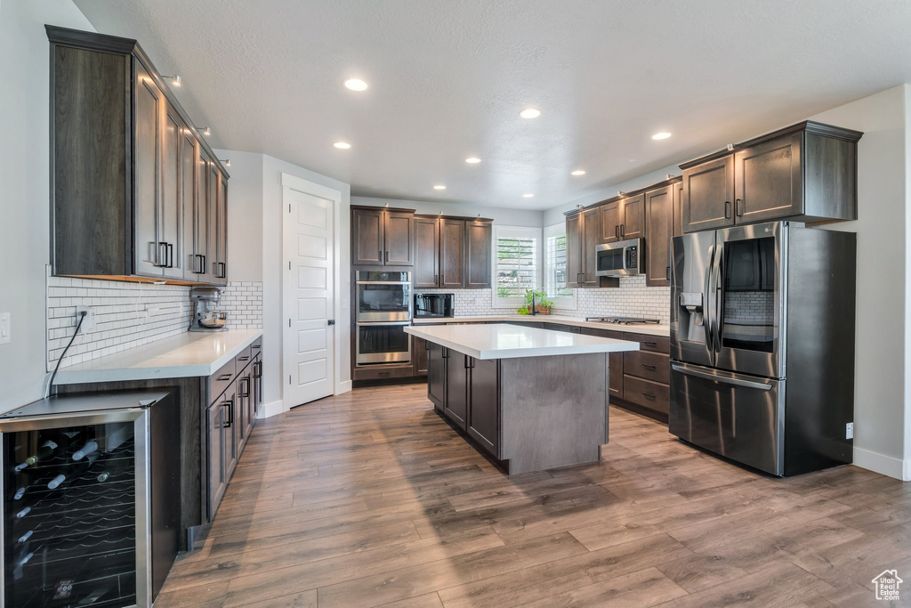 Kitchen featuring beverage cooler, appliances with stainless steel finishes, recessed lighting, light countertops, and backsplash