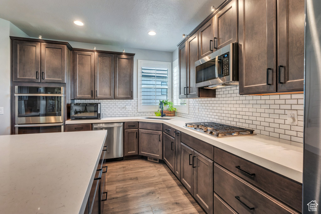 Kitchen featuring appliances with stainless steel finishes, a sink, light wood-style flooring, dark brown cabinetry, and light countertops