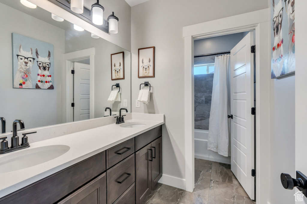 Bathroom featuring marble look tile flooring, baseboards, double vanity, and shower / bathtub combination with curtain