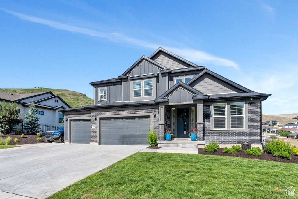 Craftsman house featuring board and batten siding, a front yard, brick siding, and a garage