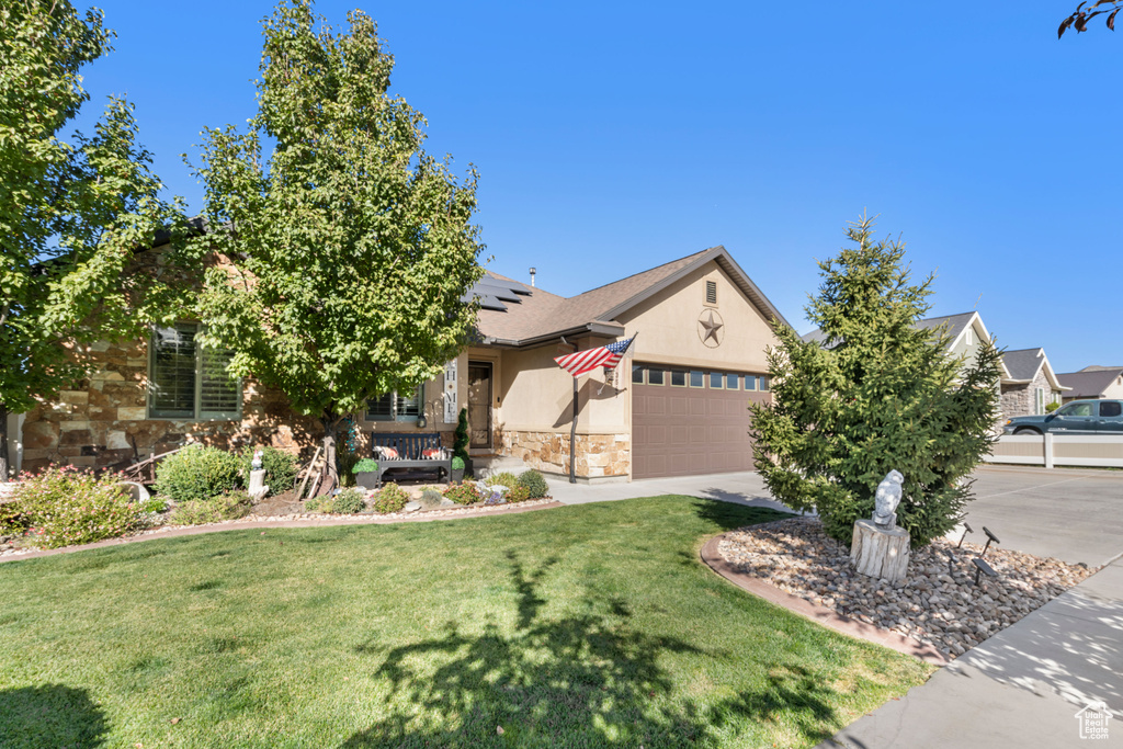Obstructed view of property featuring stone siding, a front yard, solar panels, a garage, and stucco siding