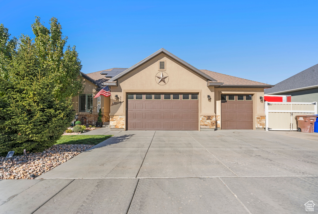 Ranch-style house with stone siding, stucco siding, an attached garage, solar panels, and concrete driveway