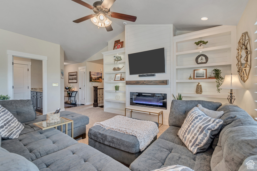 Living room with ceiling fan, light carpet, lofted ceiling, a glass covered fireplace, and built in features