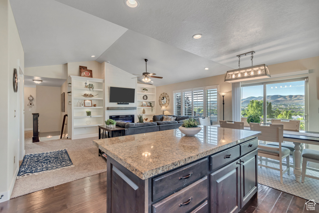 Kitchen featuring lofted ceiling, ceiling fan, dark wood-type flooring, light stone counters, and a kitchen island