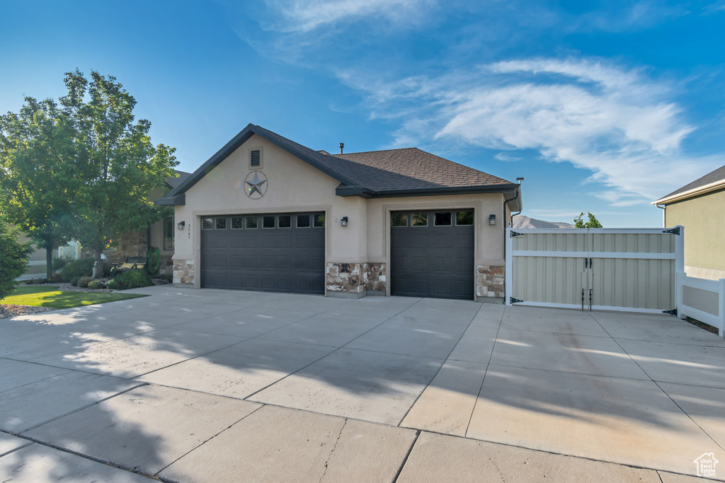 Ranch-style house featuring stucco siding, an attached garage, stone siding, driveway, and a shingled roof