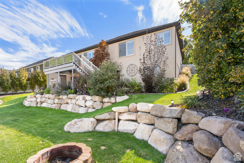 Back of property featuring a fire pit, stairway, a wooden deck, a yard, and stucco siding