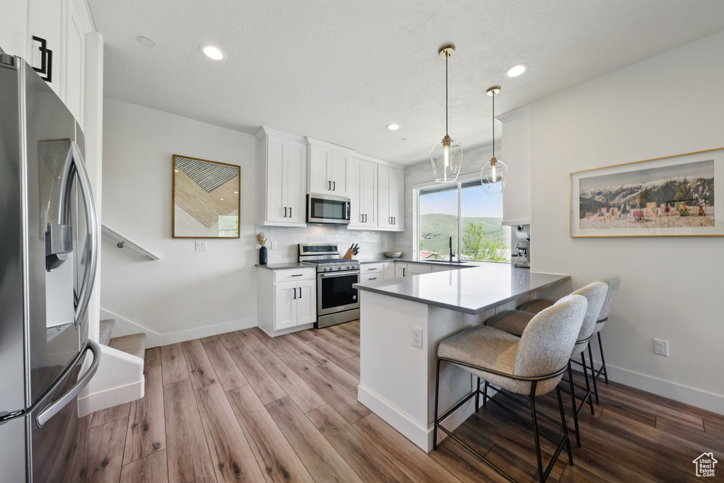 Kitchen with appliances with stainless steel finishes, a peninsula, white cabinets, wood finished floors, and recessed lighting